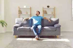 Man sitting in sun rays on the couch in the center of a minimalist living area.