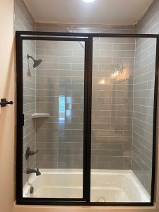 Modern dark framed shower door in a grey tiled bathroom.